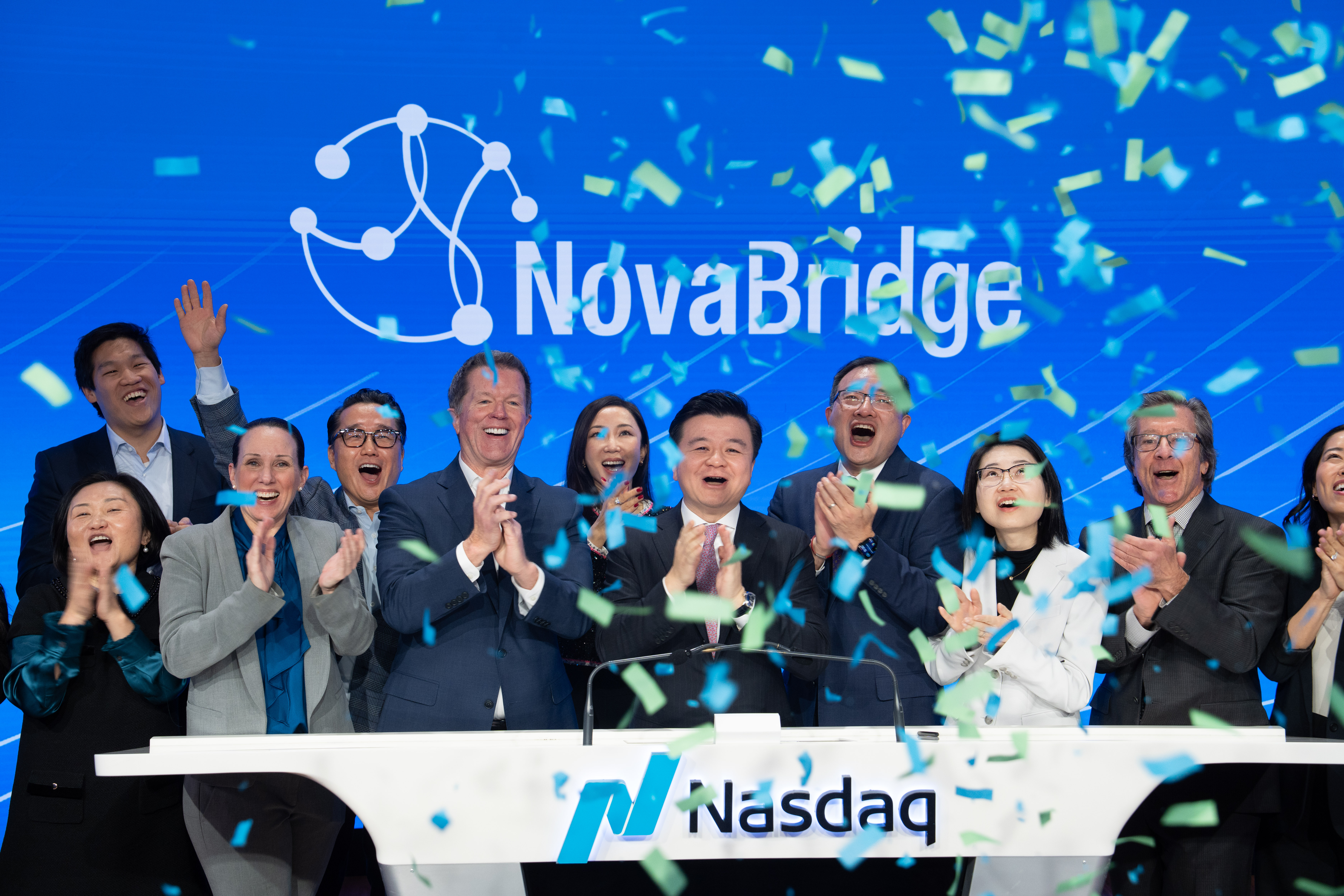Group celebrating at a Nasdaq podium with confetti falling and the NovaBridge logo on screen.